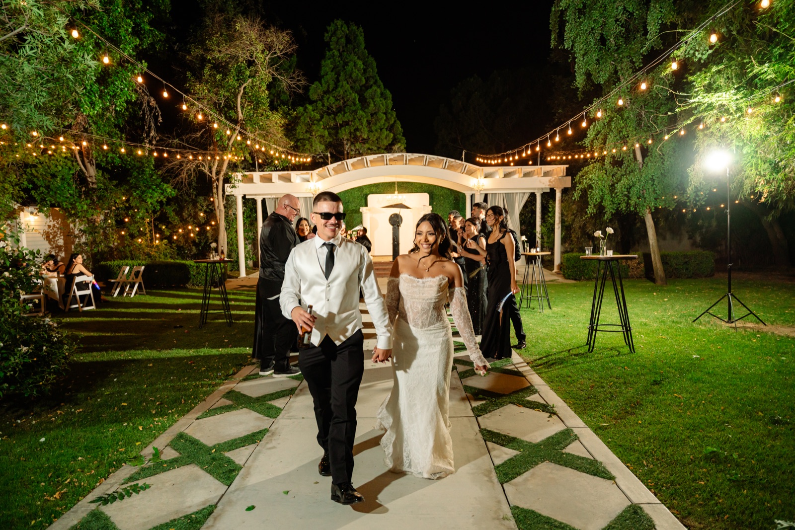 Bride and groom walking through their evening wedding reception under string lights